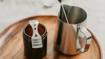 Glas mit Docht und Kanne auf Tablett.