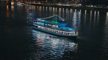 Beleuchtetes Boot fährt nachts auf Fluss.