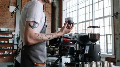 Barista holding cup near espresso machine.