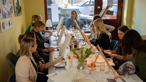 Frauen malen an Leinwänden an einem Tisch drinnen.