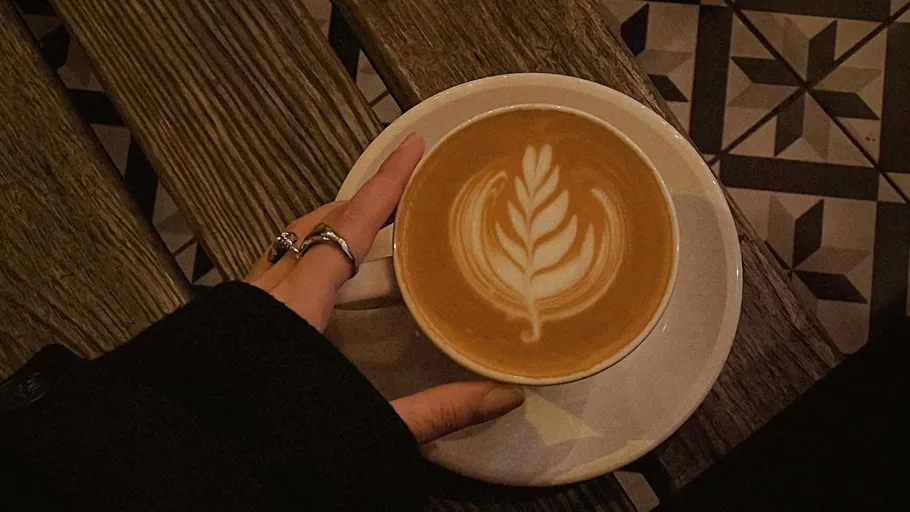 Latte with leaf art, hand on table.