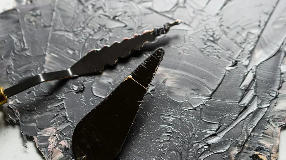 Palette knives spread gray paint on canvas.