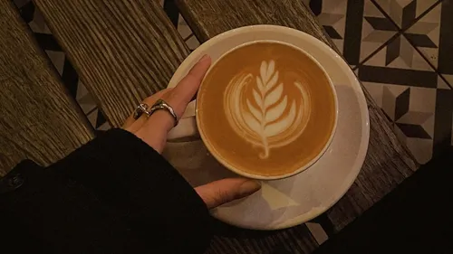 Hand holding latte with leaf art.