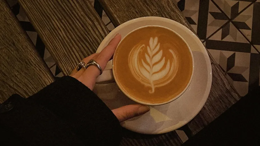 Hand hält Tasse mit Latte Art Kaffee.