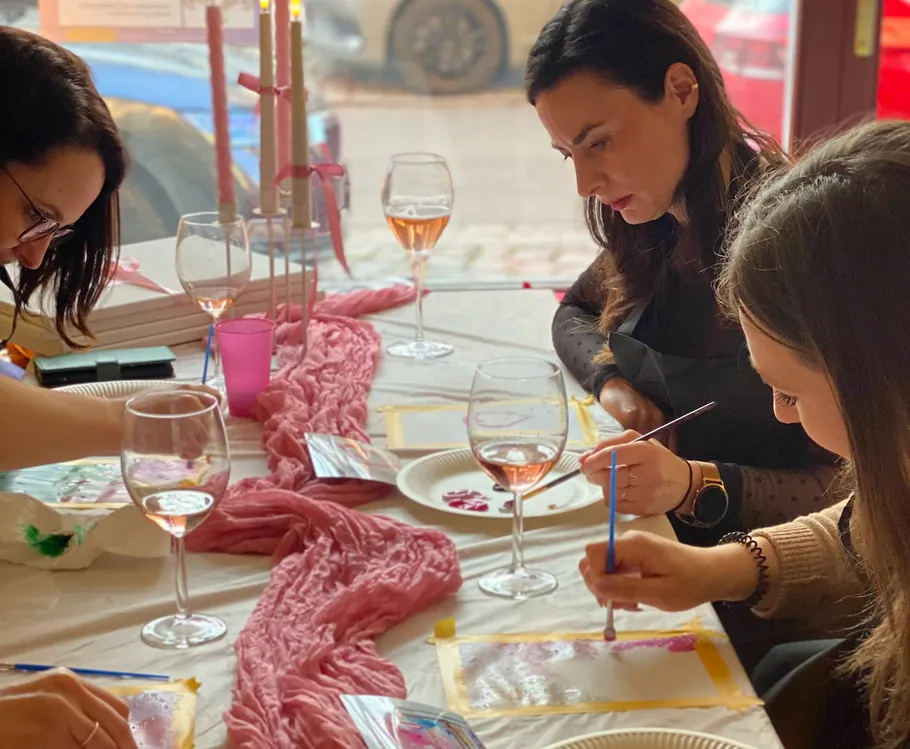 Three women painting at a table with wine.
