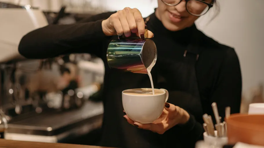 Barista pouring milk into coffee cup, smiling.