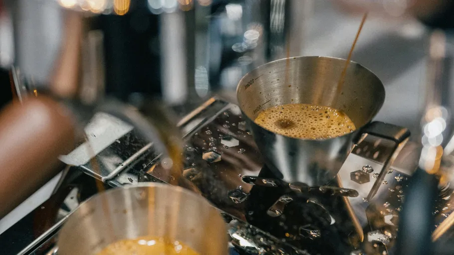 Espresso fließt in Edelstahlbecher.