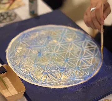 Hand painting intricate mandala on blue canvas.