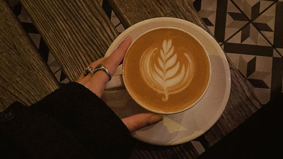 Hand holding latte with leaf art, cafe setting.