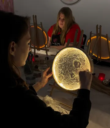Woman painting glowing moon lamp indoors.