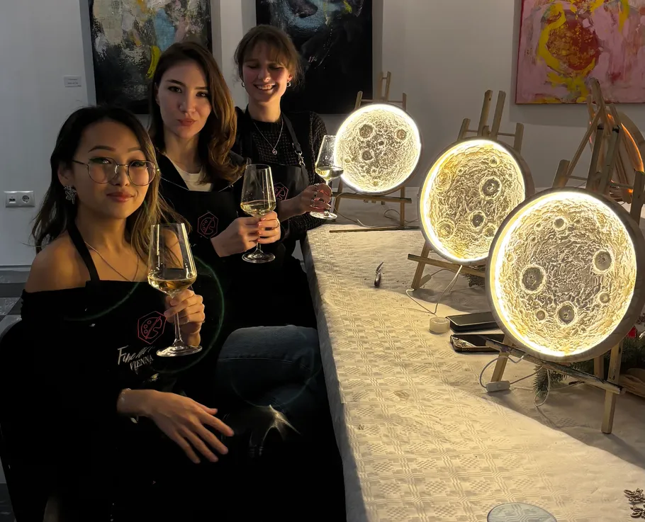 Three women holding wine glasses beside illuminated artworks.