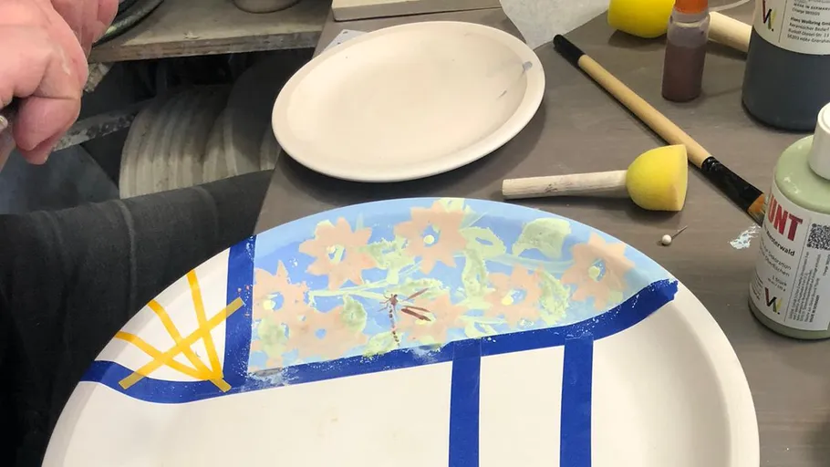 Hand painting a ceramic plate on table.