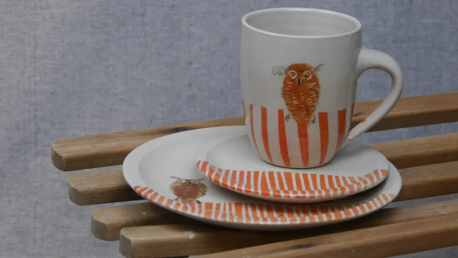 Eulenmuster-Tasse und Teller auf Holzbänken.