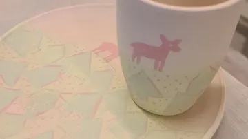 Decorative cup on patterned plate, pastel colors.