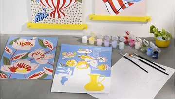 Art supplies and colorful paintings on table.