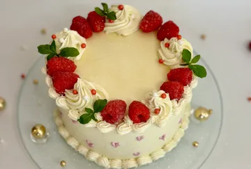 Dekorierte Torte mit Himbeeren auf weißer Oberfläche.