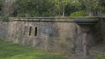 Alte Steinmauer mit Plakette im Park.