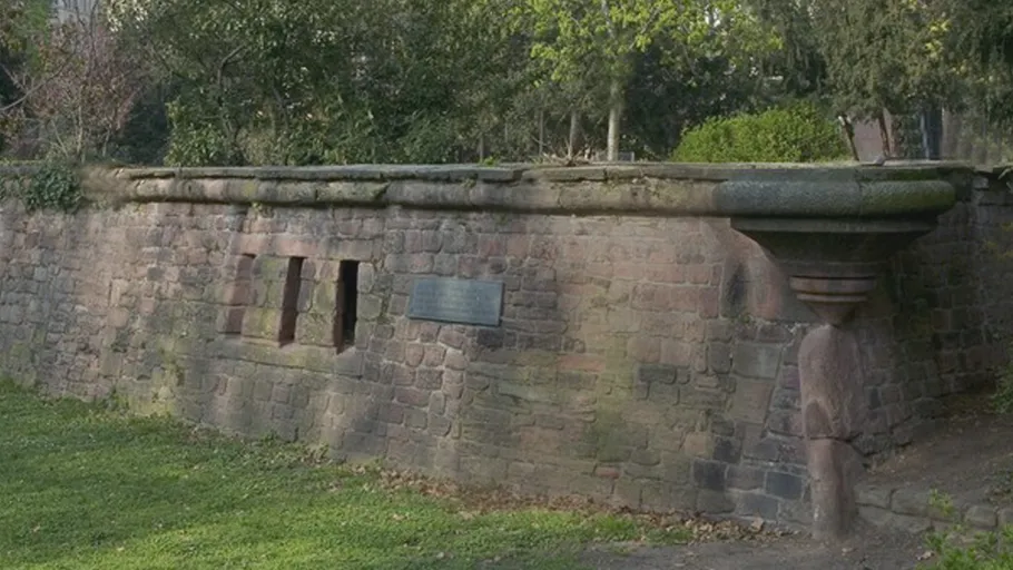 Alte Steinmauer mit Plakette im Park.