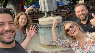 Vier Personen lächeln bei Brunnenstatue.