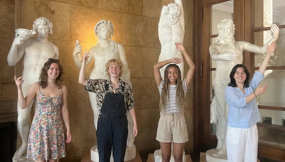 People mimic poses of marble statues indoors.