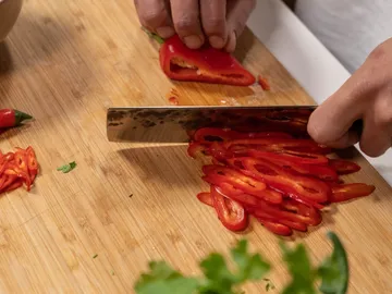 Sharp knives cut red peppers on a wooden board.