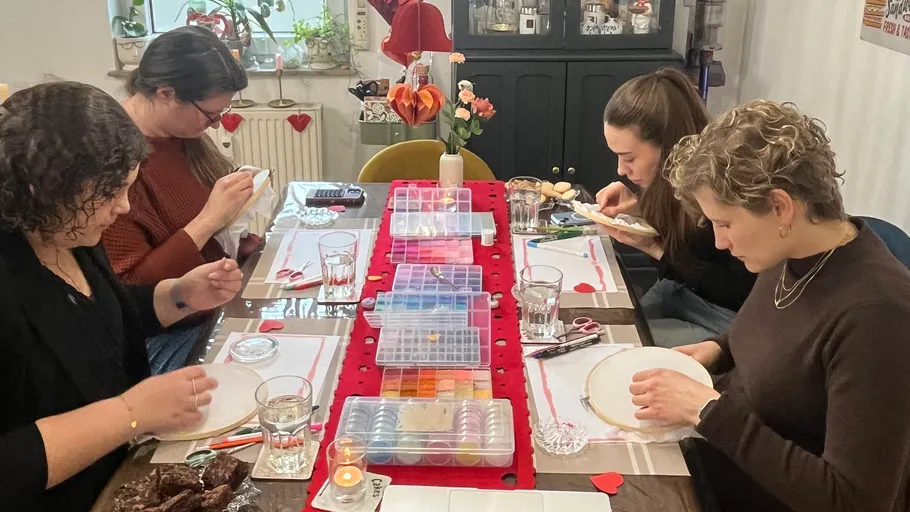 Four women engaged in embroidery at dining table.