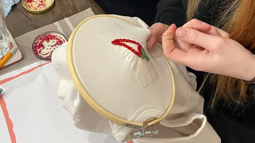 Person embroidering red chili on white fabric.