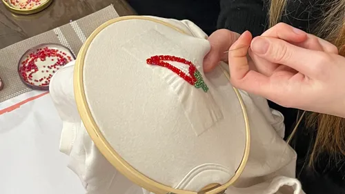 Person stickt rote Chili auf weißem Stoff.