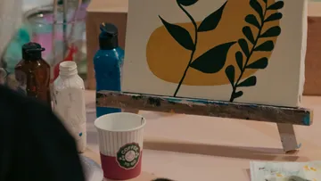 Staffelei mit abstrakter Pflanzenmalerei, Kaffeetasse in der Nähe.