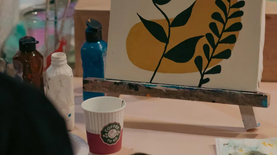 Easel with abstract plant painting, coffee cup nearby.