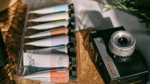 Acrylic paints and vintage camera on woven surface.