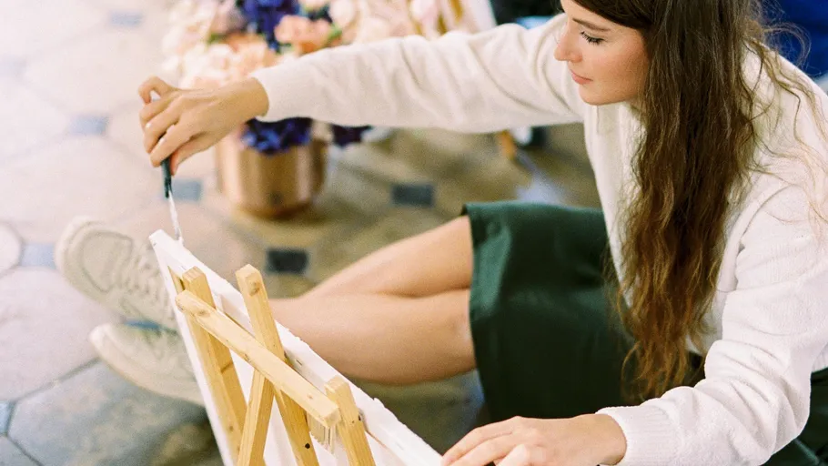 Woman painting on canvas, flowers nearby.