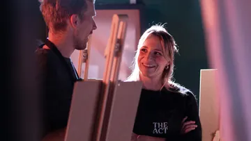 Two people talking with easels in art studio.