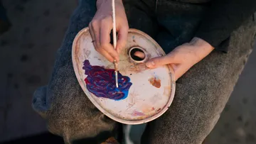 Hand mischt Farben auf einer Palette.
