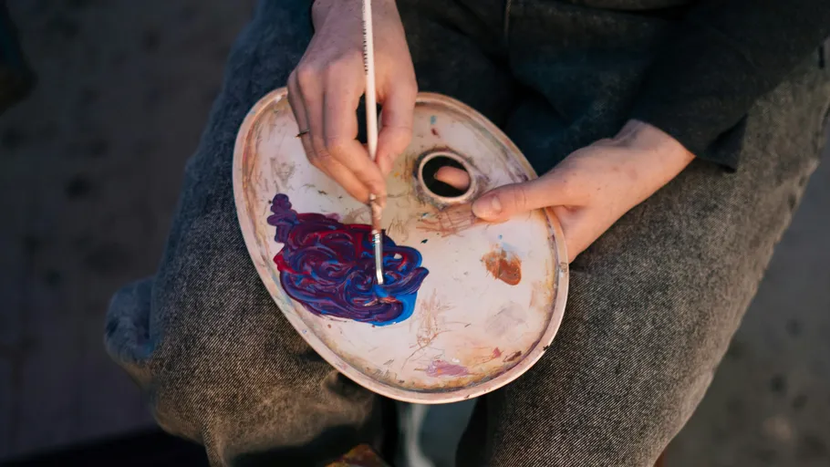 Hand mischt Farben auf einer Palette.