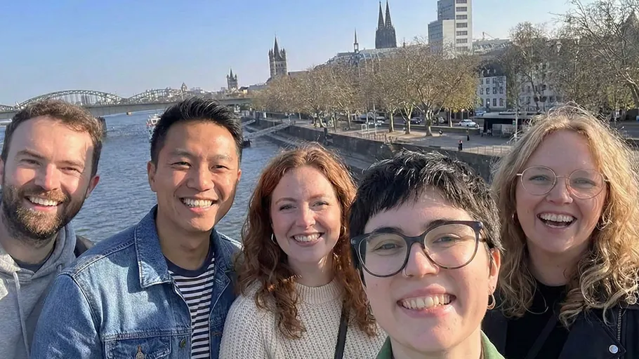 Fünf Menschen lächeln auf einer Brücke, Stadt im Hintergrund.
