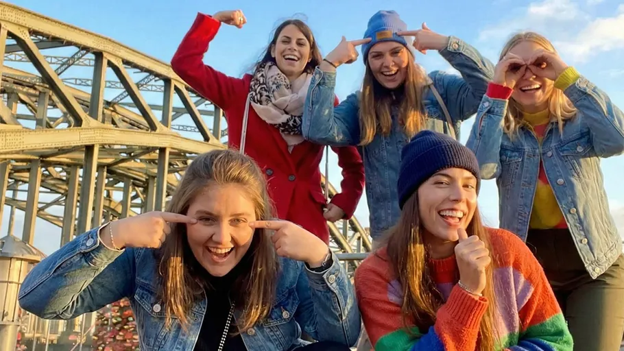Fünf Frauen posieren fröhlich auf einer Brücke.