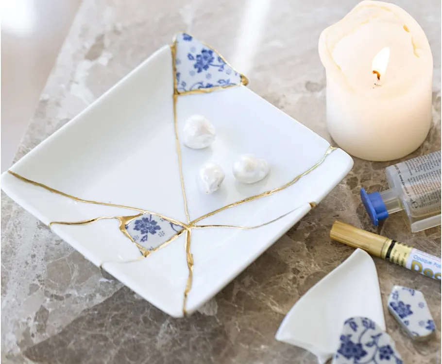 Repaired plate with gold seams, beside a candle.