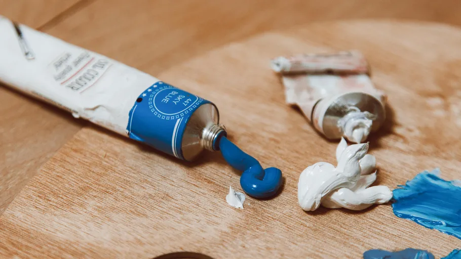 Blaue und weiße Farbtuben auf Holzoberfläche.