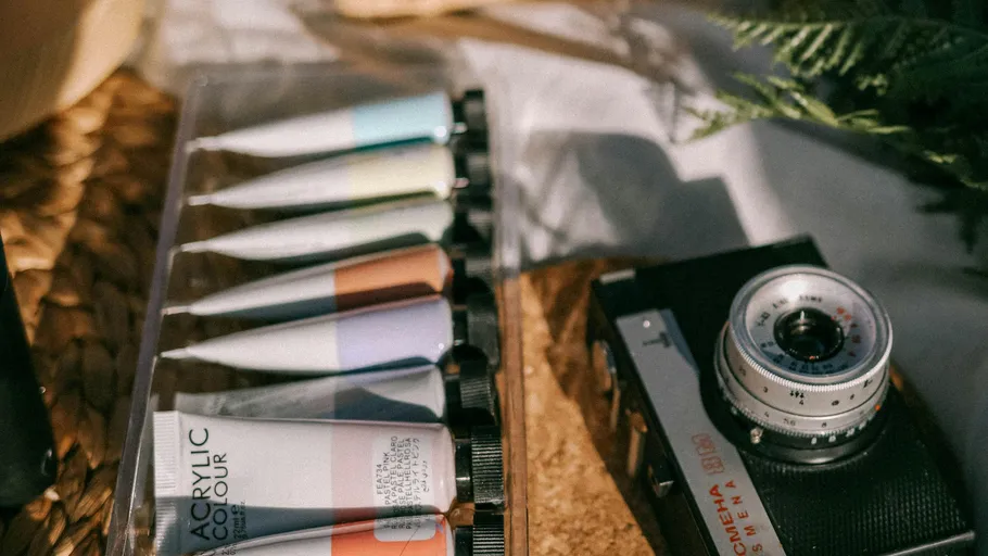 Paint tubes and camera on woven surface.