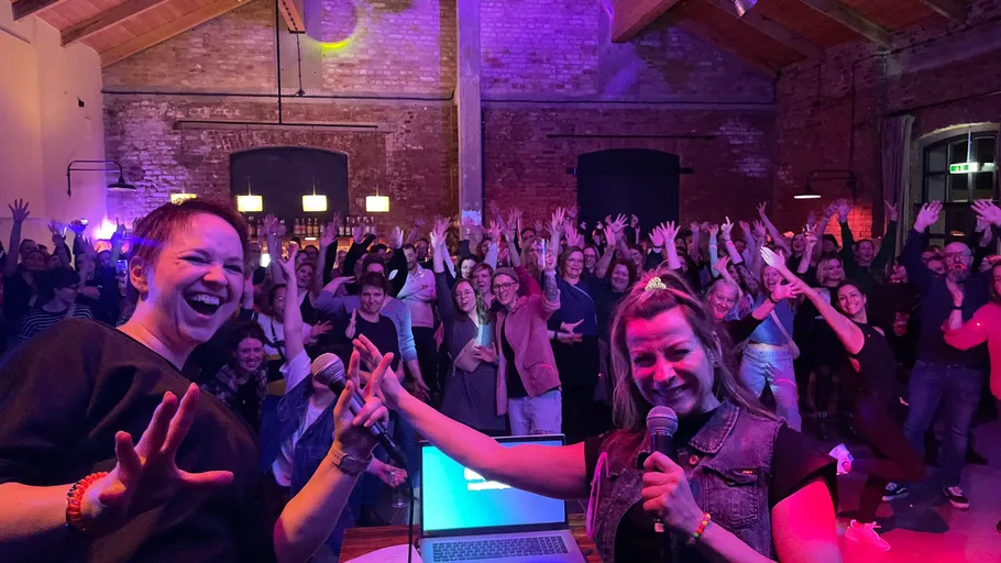 Two women hosting lively indoor event with crowd.