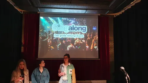 Drei Personen stehen vor einem Singalong-Event-Schild.