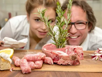 Meat and ingredients are looked at by smiling people.