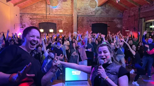 Zwei Frauen singen, Menge jubelt im Hintergrund.