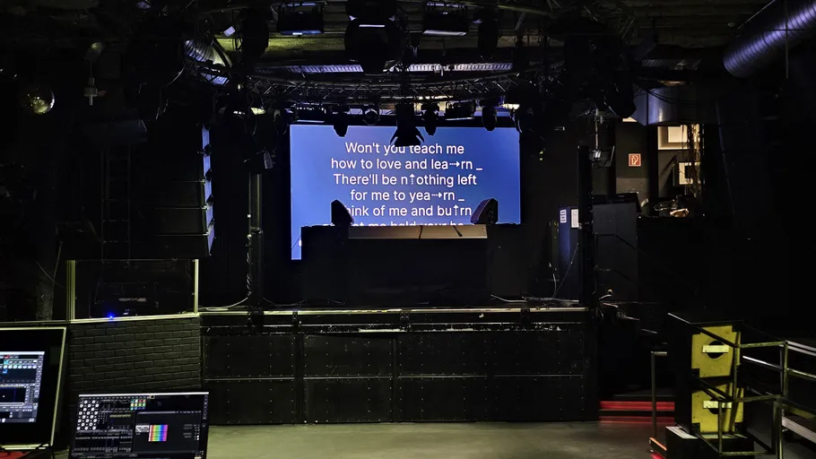 Empty club stage with song lyrics displayed.