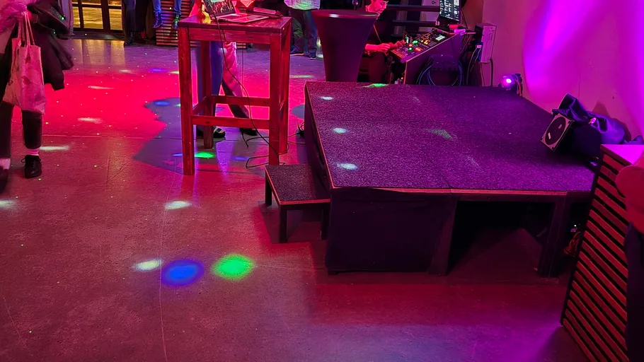 Kleine Bühne mit bunten Lichtern in einem Veranstaltungsort.