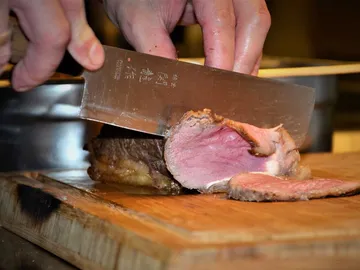 A cook cuts a piece of meat on a board.
