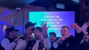 Gruppe singt Karaoke, Text auf Bildschirm.