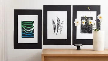 Drei abstrakte Kunstwerke an Wand über Tisch.