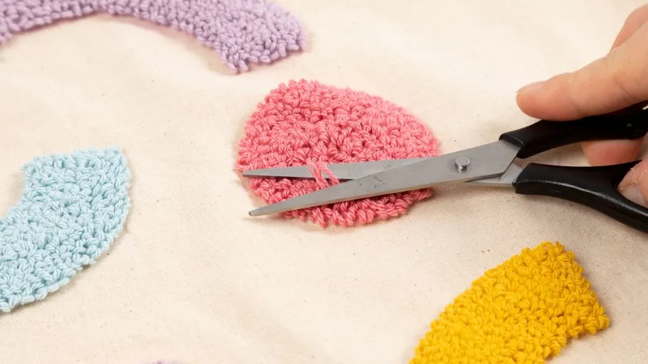 Scissors trimming pink crochet patch on fabric.